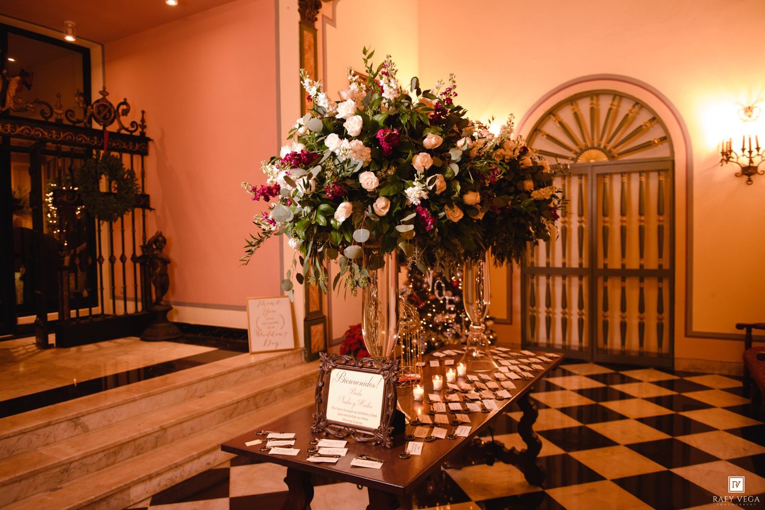 Elegant wedding venue lobby with tall floral arrangement of pink and white flowers on a checkered marble floor.