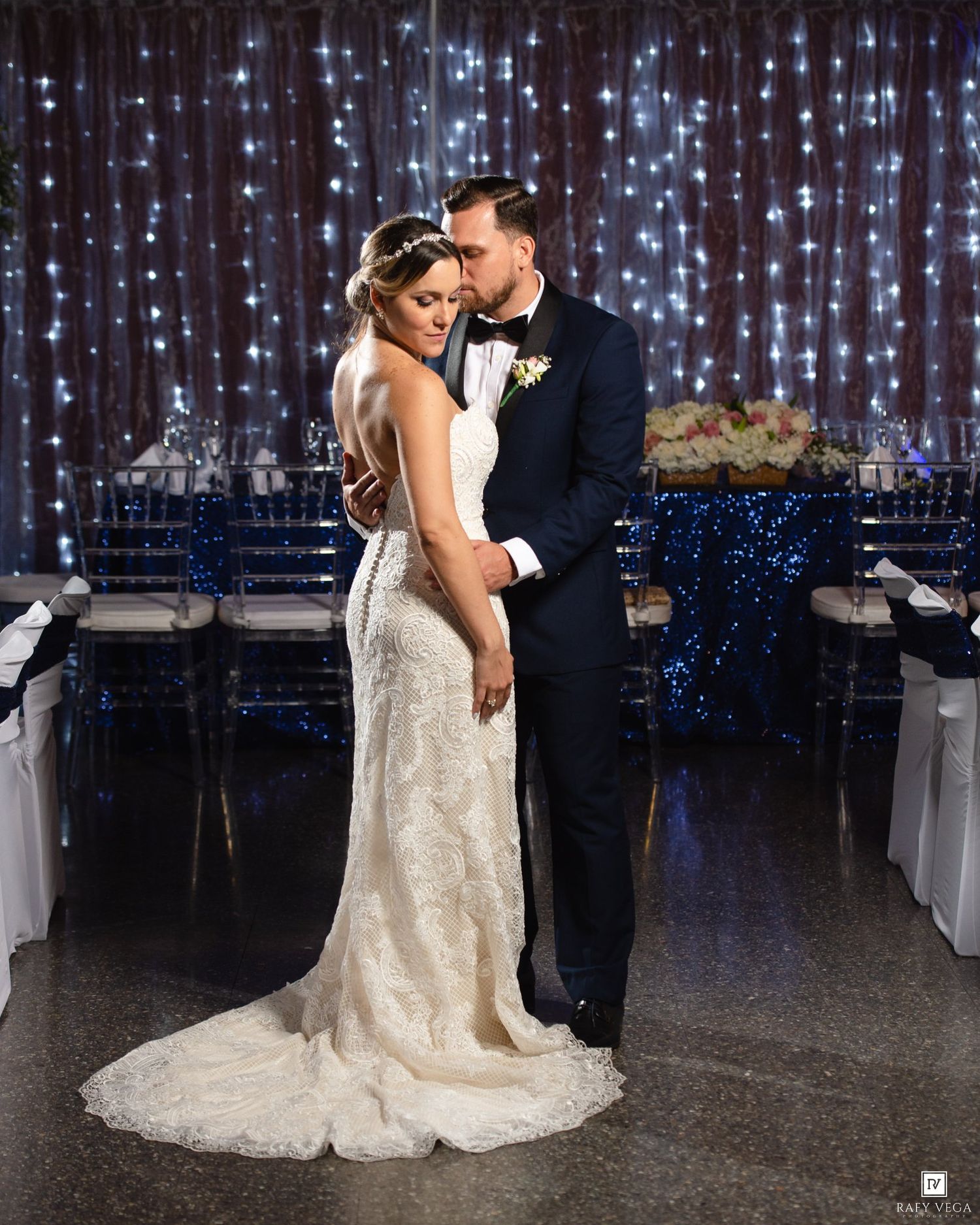 Bride and groom share a romantic moment in front of a twinkling fairy light backdrop at their elegant wedding reception.