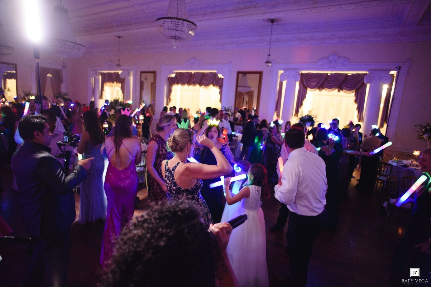 Wedding reception guests dancing with colorful glow sticks in an elegant ballroom venue.