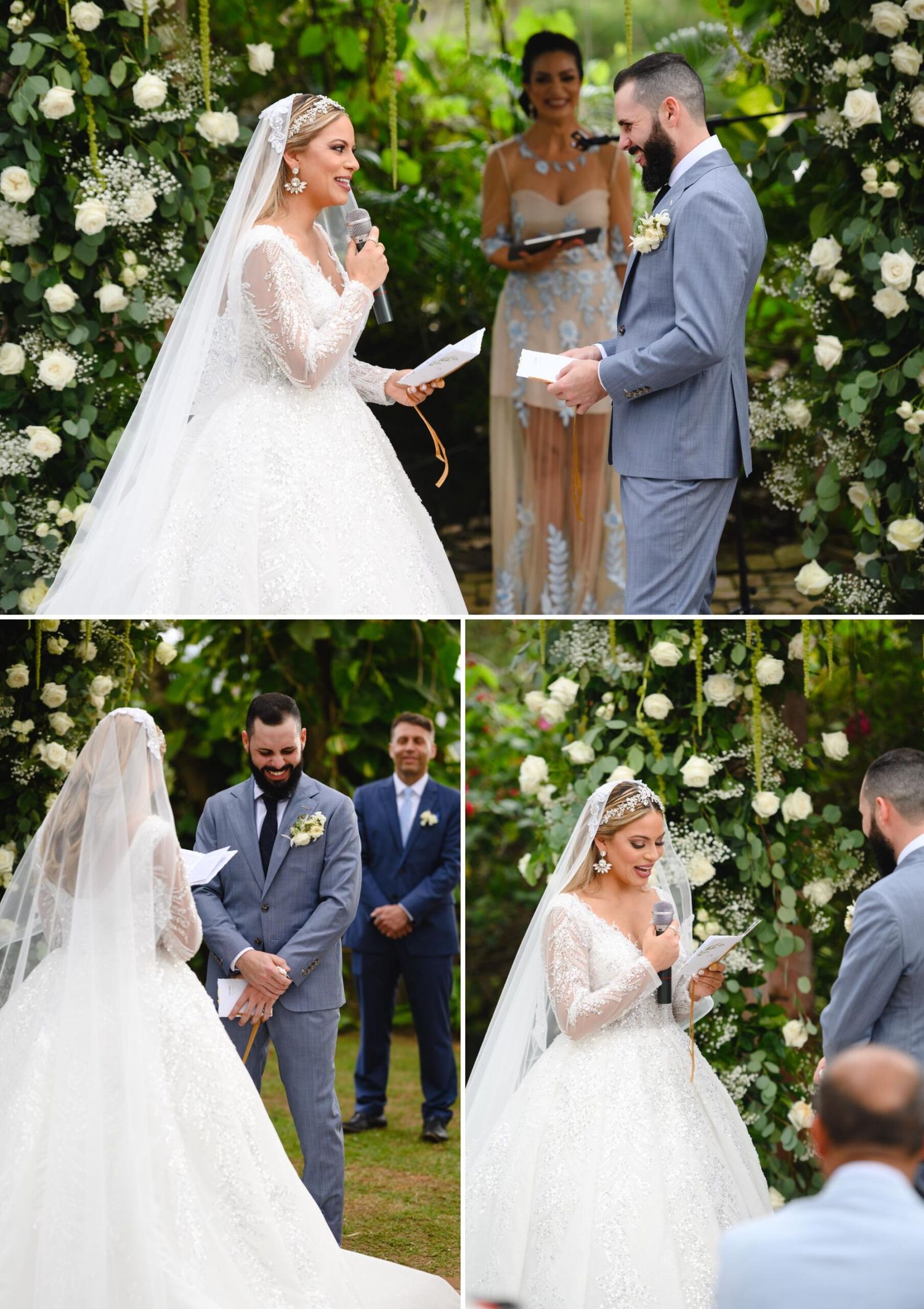 Bride in lace gown reads vows to groom in gray suit at outdoor wedding ceremony with white floral arch.