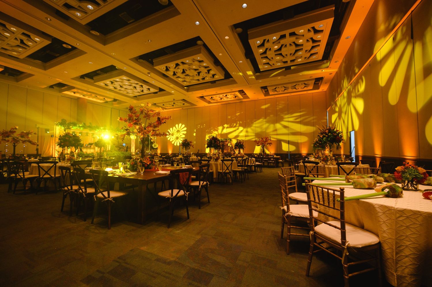 Elegant banquet hall with golden lighting, floral centerpieces, and decorative projected patterns on walls for a special event.