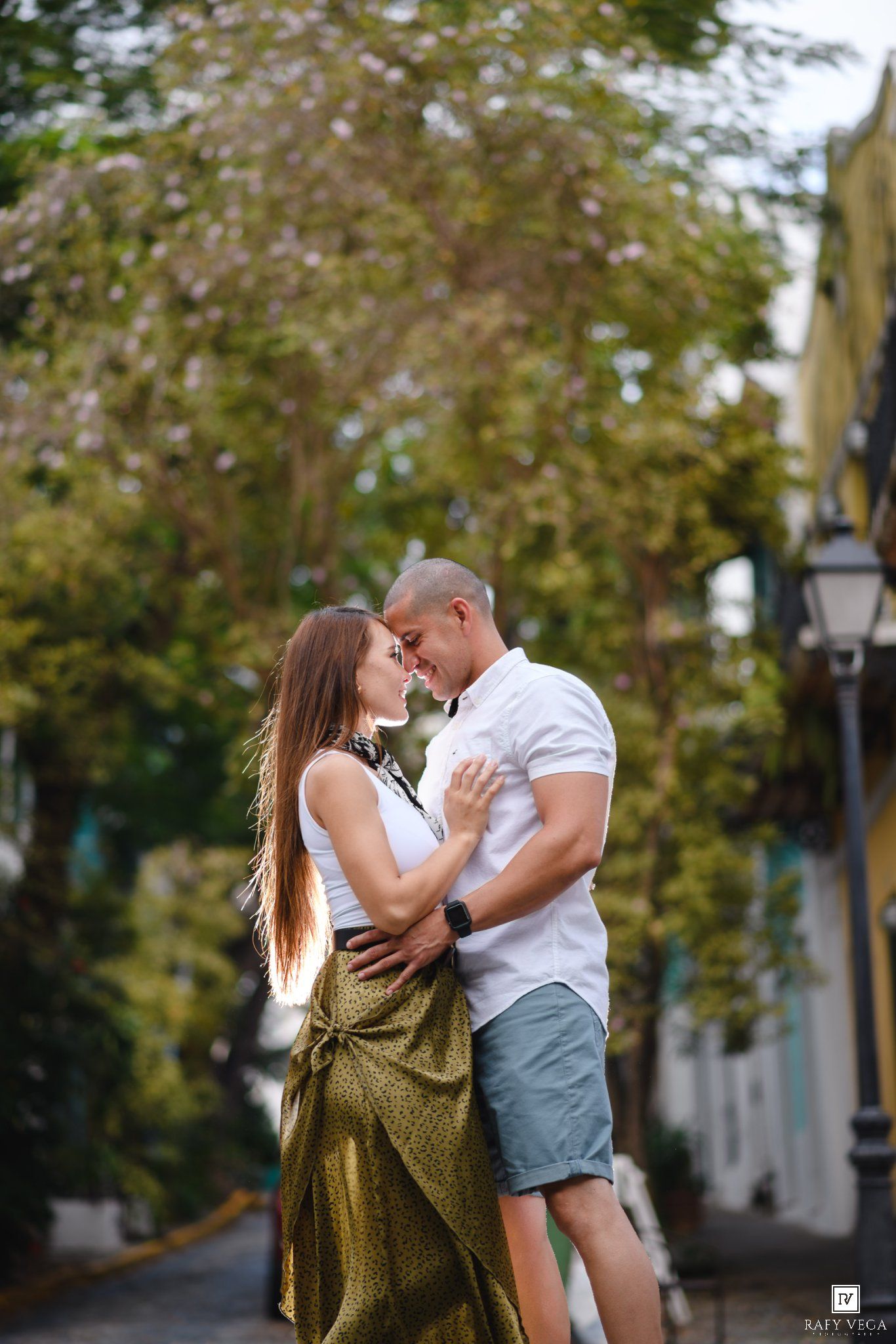 Romantic couple embracing and almost kissing on a charming tree-lined street outdoors.