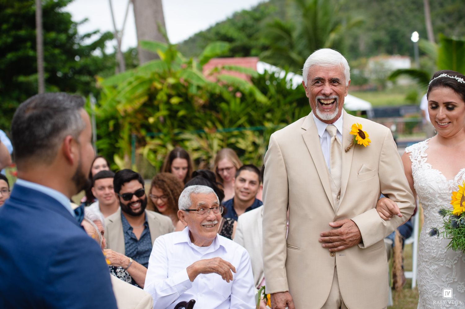 Joyful father walks bride down the aisle at outdoor wedding ceremony, with guests smiling in background.