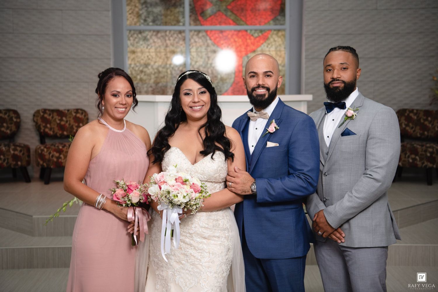 Wedding party of four poses together, bride in lace gown with bouquet flanked by bridesmaid and groomsmen.