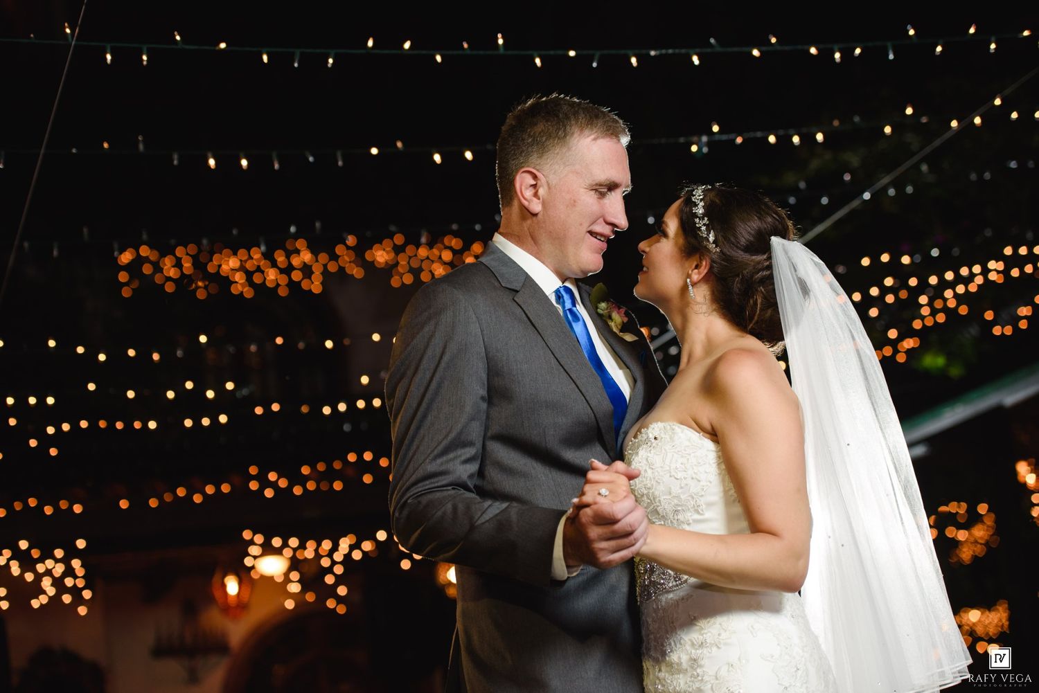 Bride and groom share first dance under romantic string lights at elegant outdoor wedding reception.