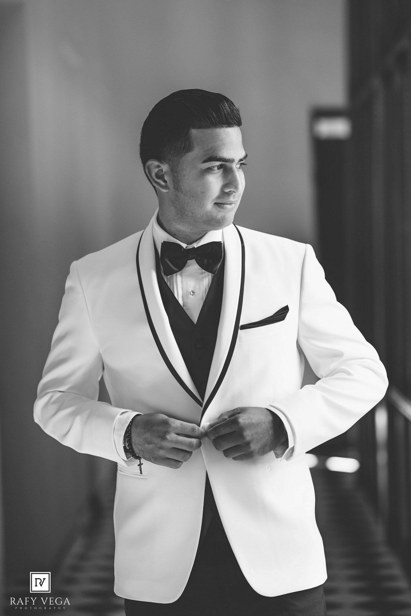 Black and white photo of a young man in a white tuxedo jacket with bow tie, adjusting his suit jacket.