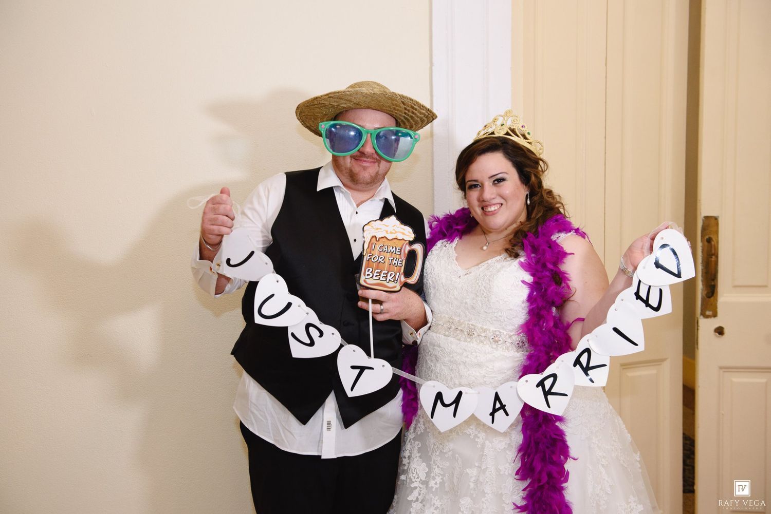 Newlyweds pose at wedding photo booth with Just Married banner, fun props and colorful feather boa.