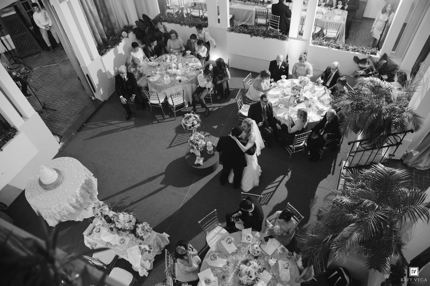 Aerial black and white photo of elegantly dressed guests dancing and dining at a formal wedding reception.