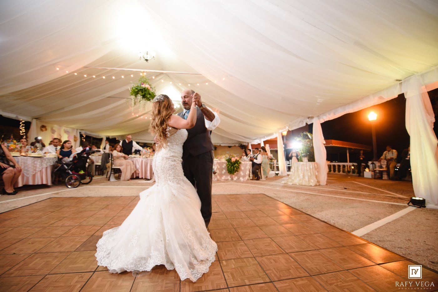 Bride and groom share an elegant first dance under a white draped tent with warm evening lighting at their wedding reception.
