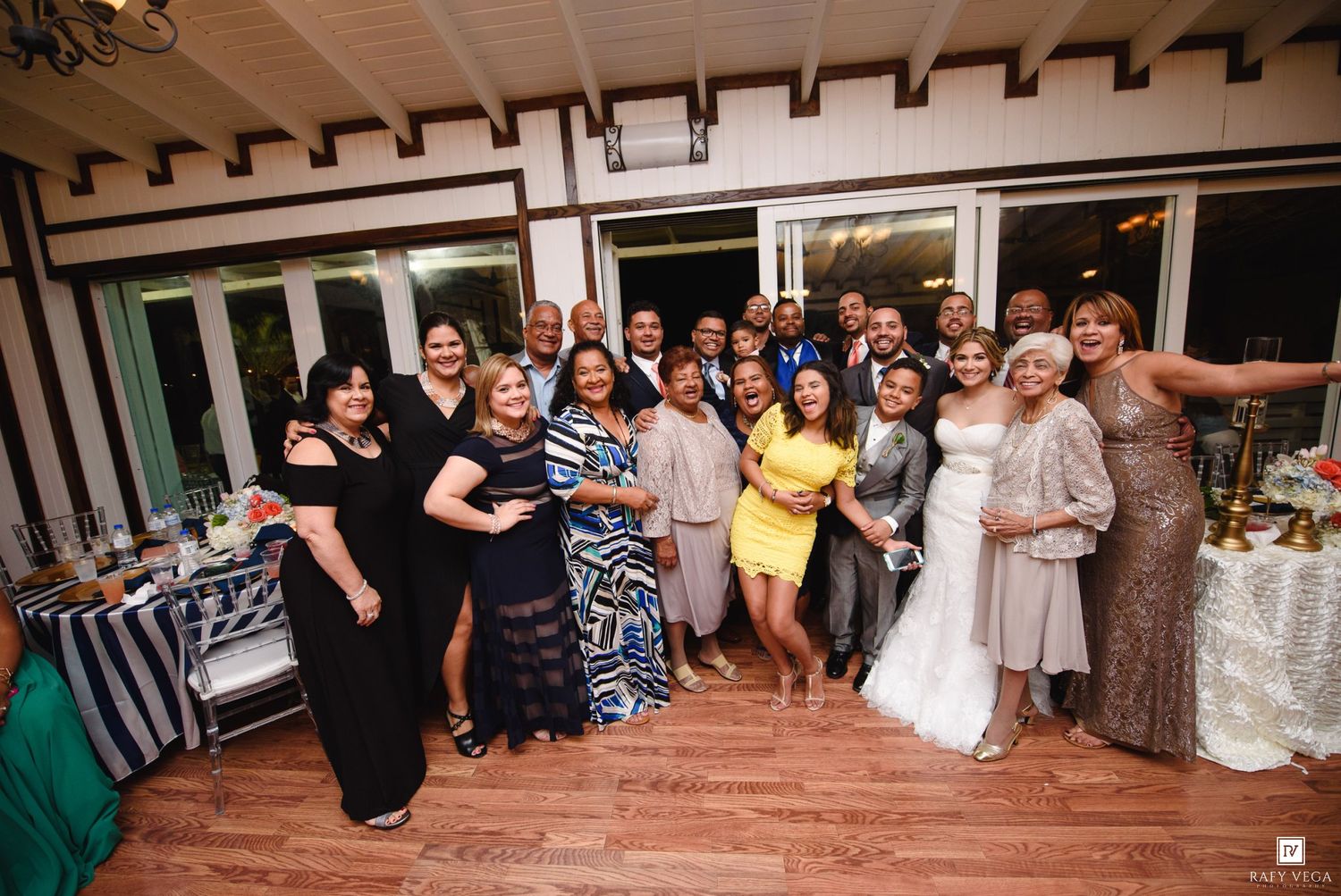 Large group of wedding guests and bride pose together for a joyful photo at the reception venue.