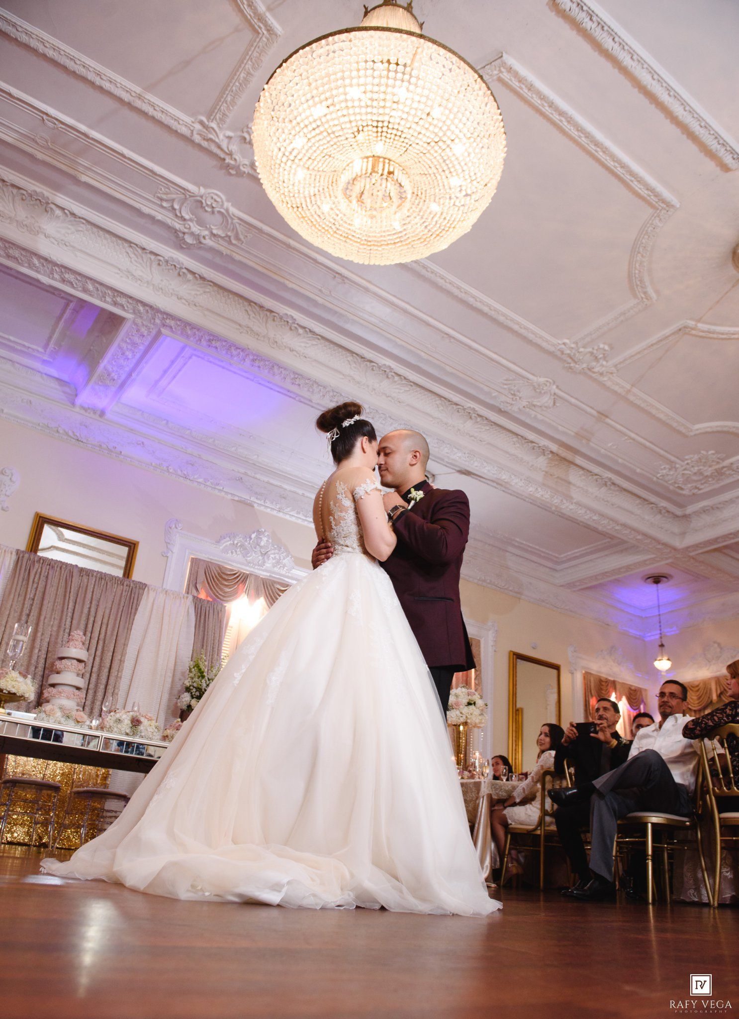 Bride and groom share first dance under crystal chandelier in elegant ballroom at wedding reception.