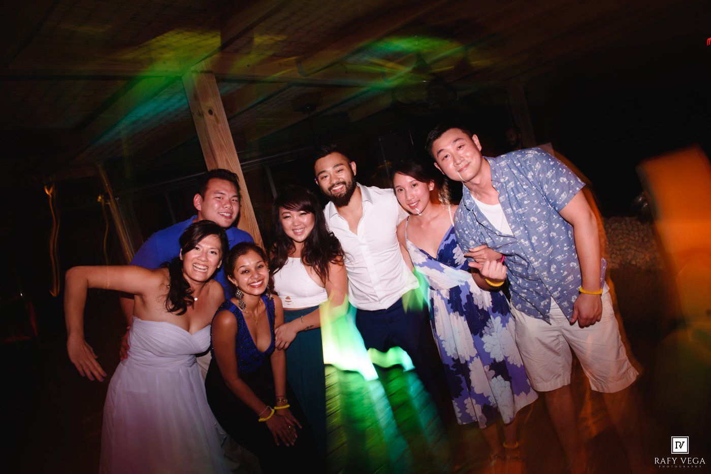 Group of friends posing together at a festive party with colorful lights on a dance floor.