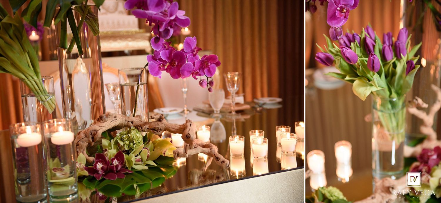 Elegant wedding reception table with purple orchids, tulips, and glowing candles in glass vases on a mirrored surface.