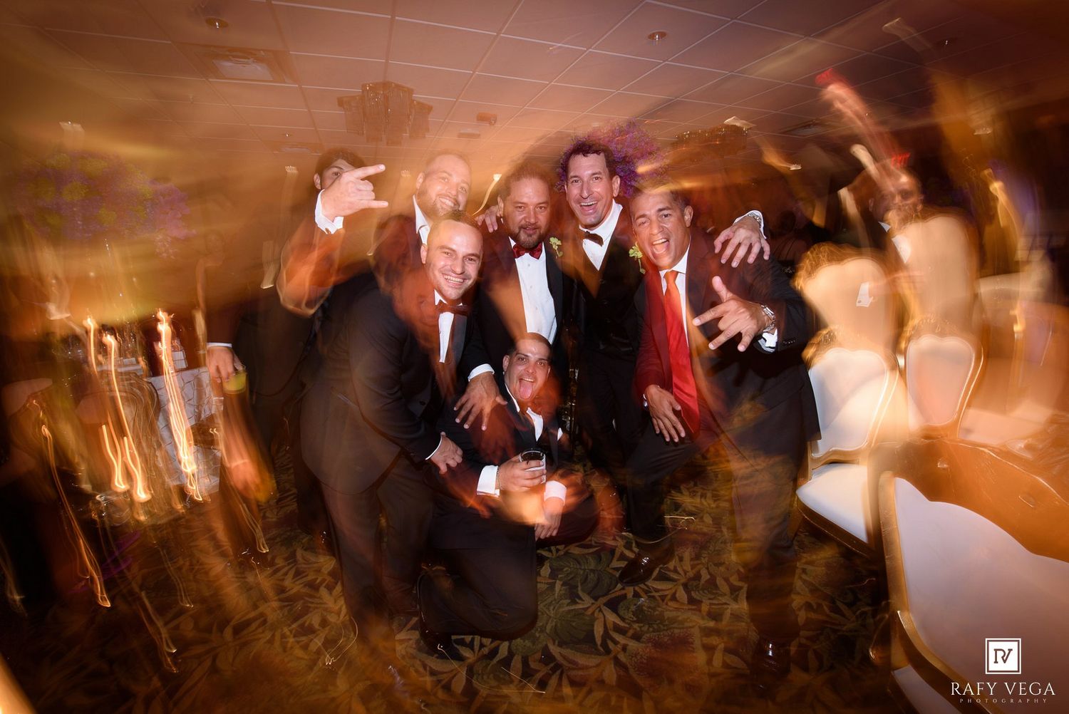 Group of men in formal attire posing together at a wedding reception party with motion blur effect.