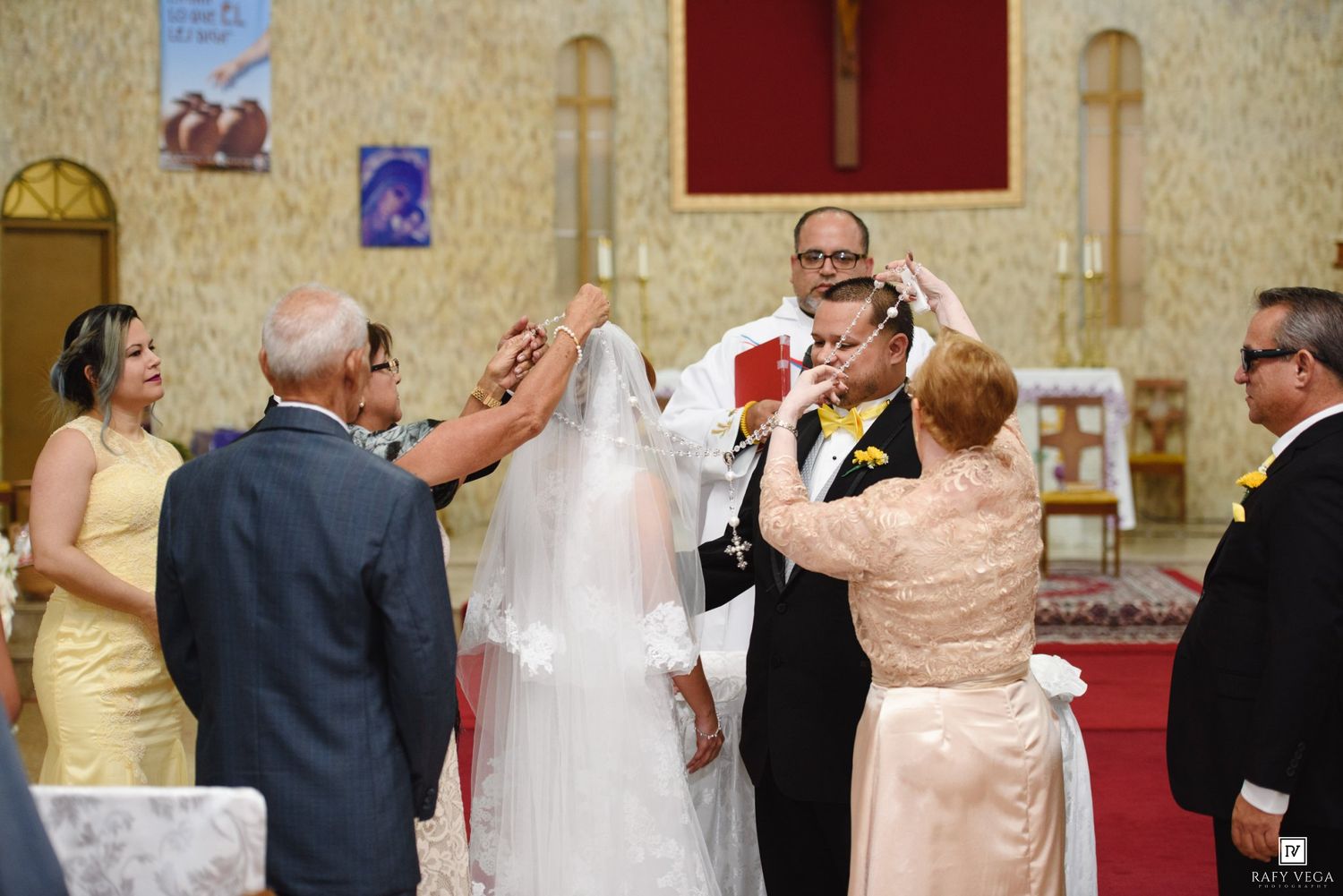 Wedding ceremony in church with bride, groom, and family members during traditional veil ritual.