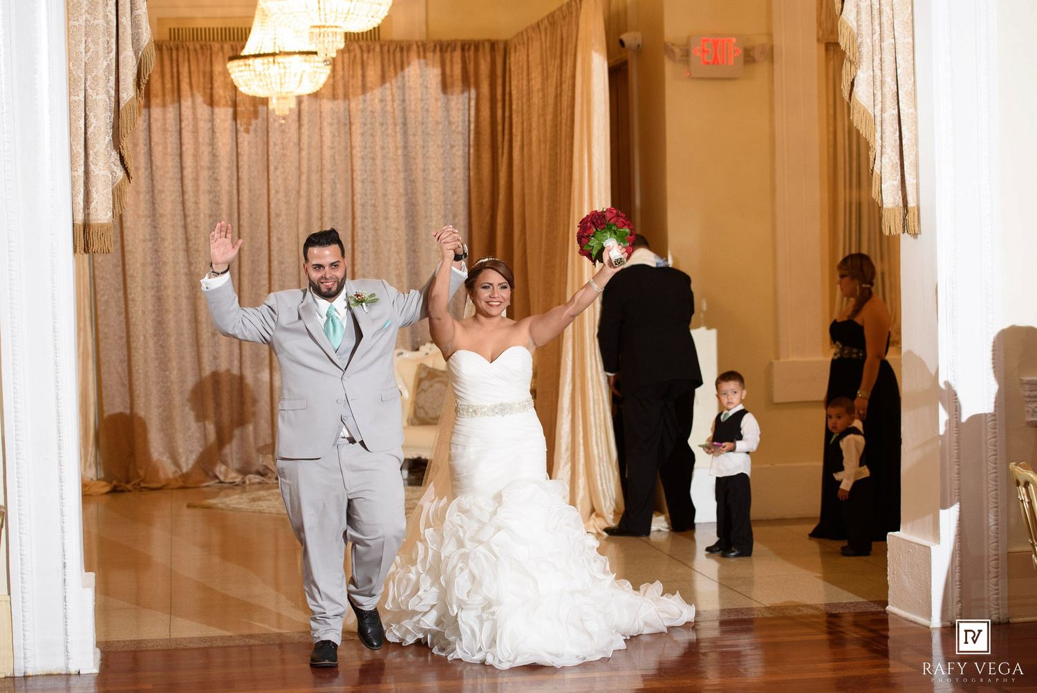 Bride and groom celebrate grand entrance at elegant wedding reception venue with guests watching nearby.