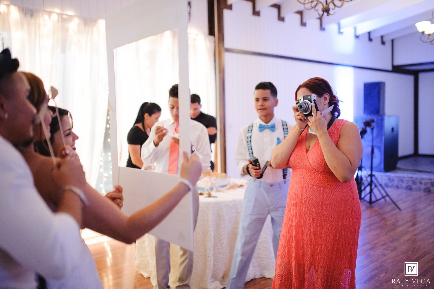 Wedding guests photograph moments at a vibrant reception with decorative curtains and warm lighting.