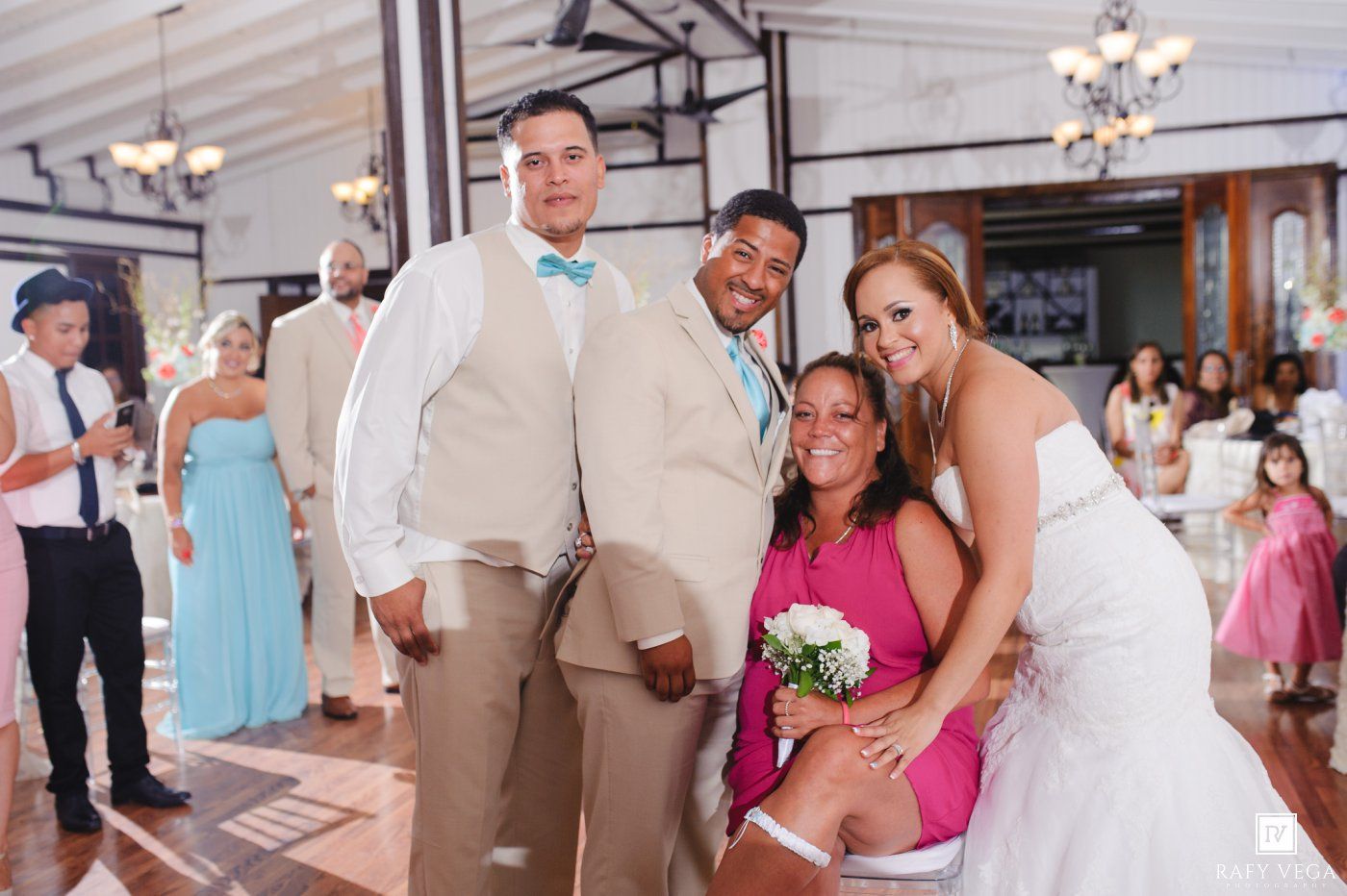 Bride and groom pose with smiling guests at indoor wedding reception venue.
