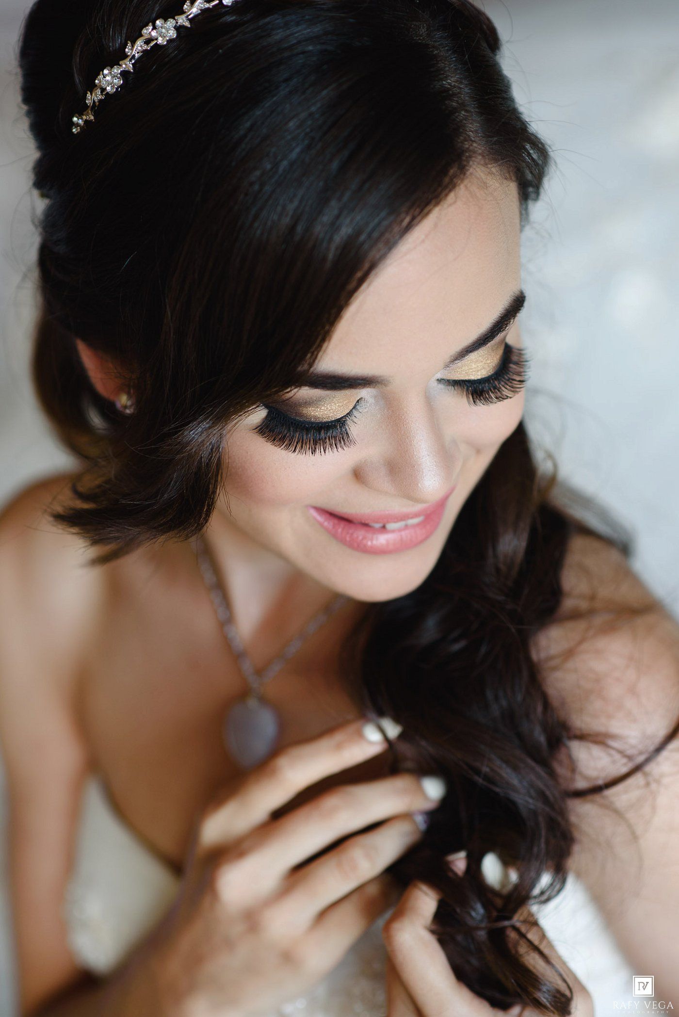 Elegant bride with dark hair, tiara, dramatic lashes, and soft pink makeup looking down gracefully.