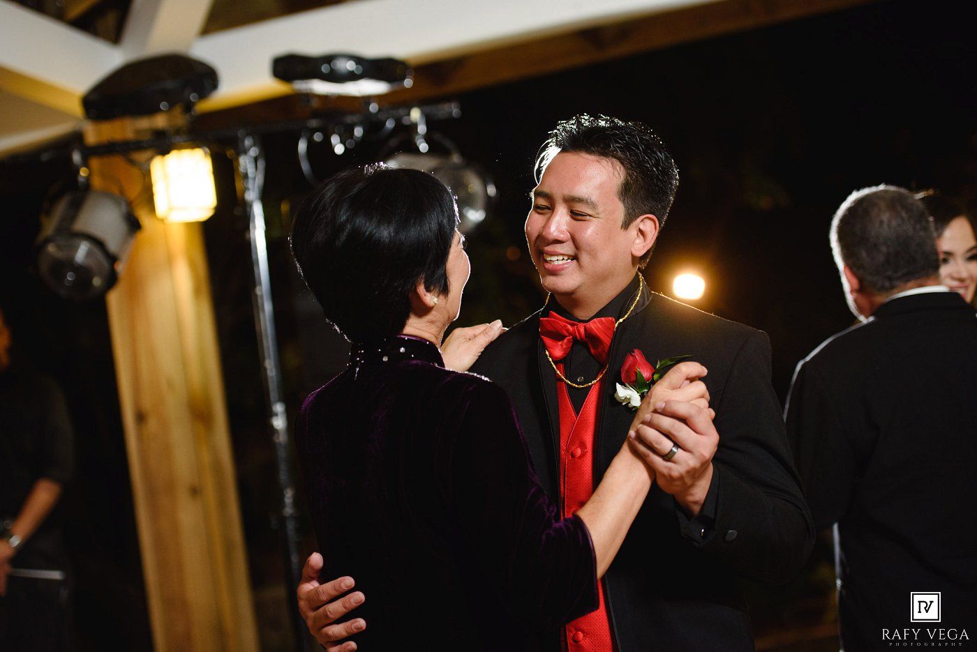 Couple dancing elegantly at a wedding reception, man in black tuxedo with red bow tie and boutonniere.