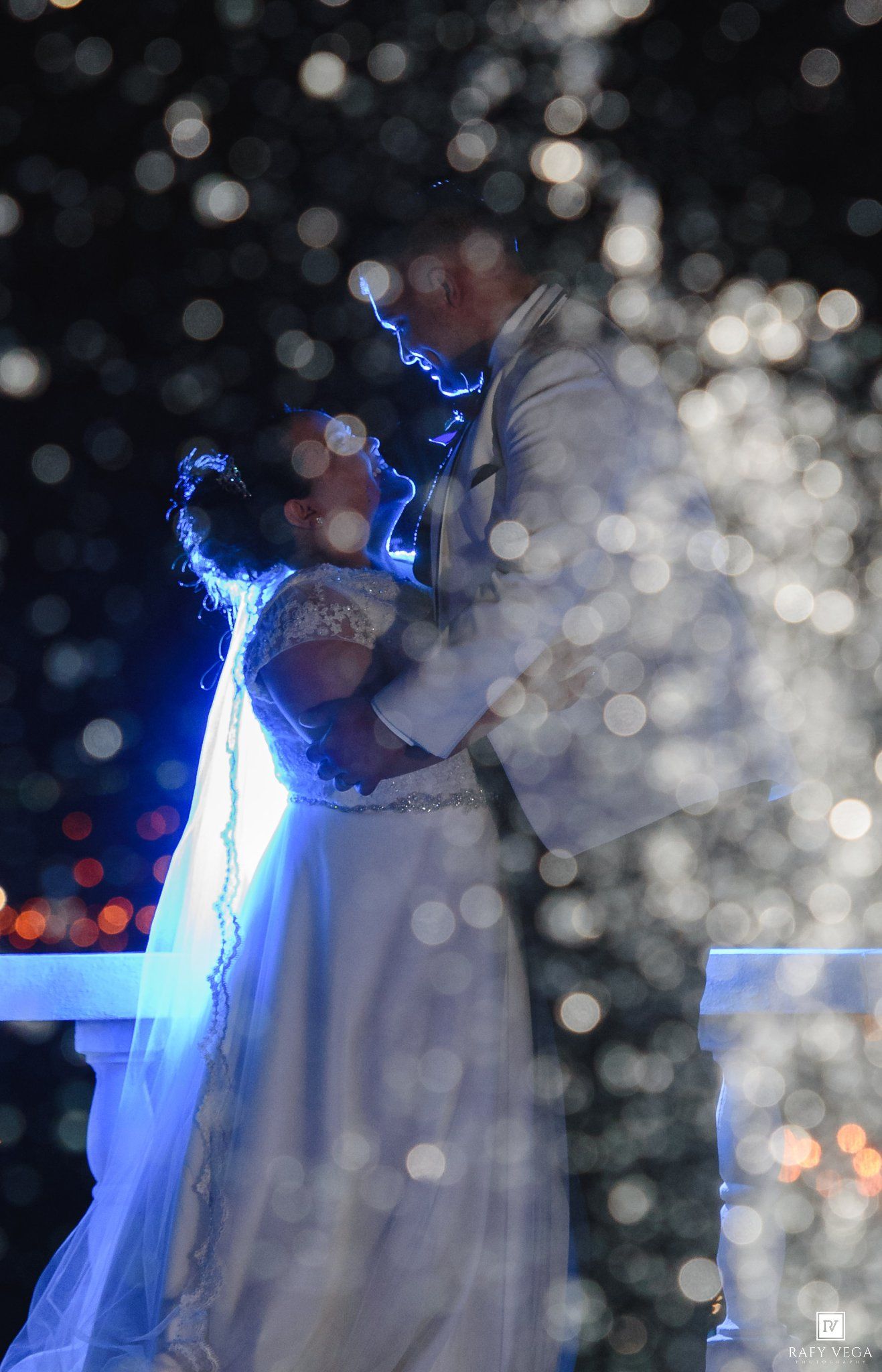 Bride and groom share a romantic moment at night, surrounded by sparkling bokeh lights in a dreamy wedding portrait.
