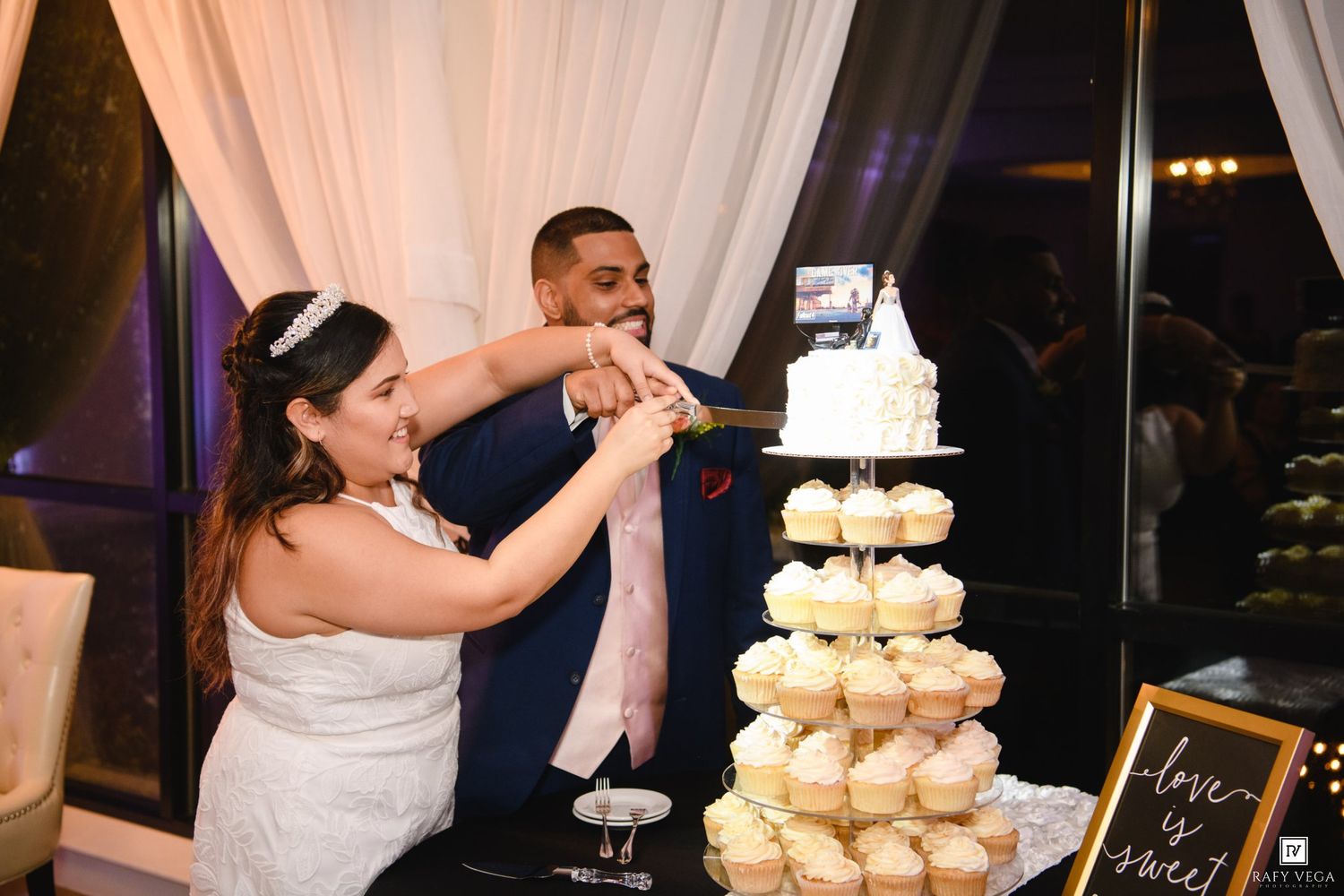 Bride and groom cutting their wedding cake at a elegant reception with cupcake tower display.
