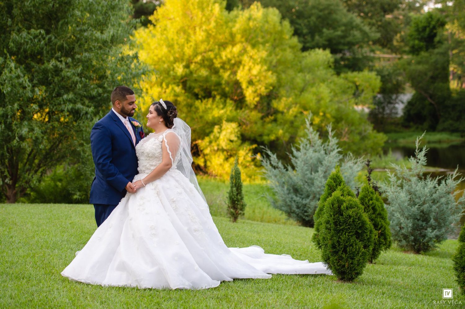 Bride and groom share a romantic moment in a lush green garden with vibrant yellow autumn trees.