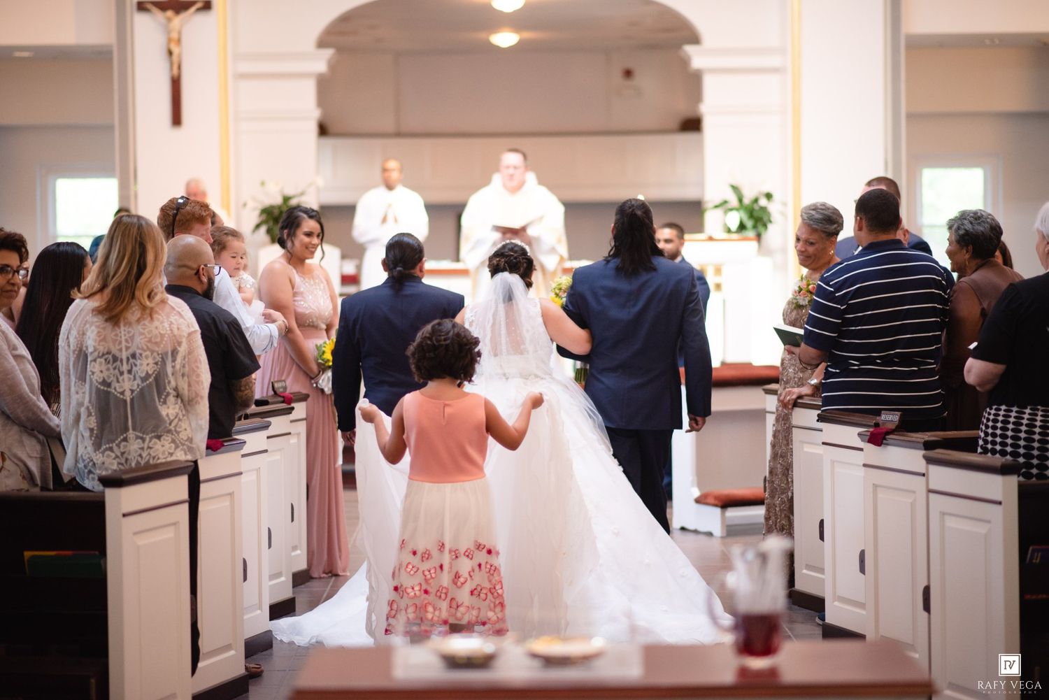 Bride and groom walk down the aisle of a church during their wedding ceremony with a flower girl.