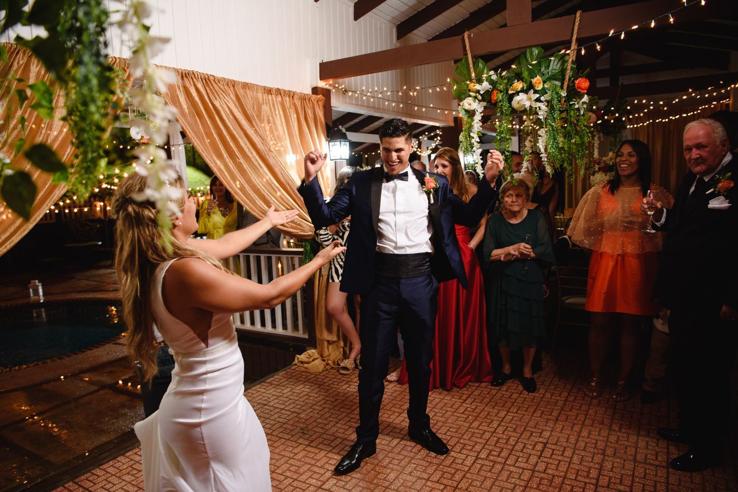 Bride and groom share joyful first dance at elegant indoor wedding reception with string lights and floral decor.