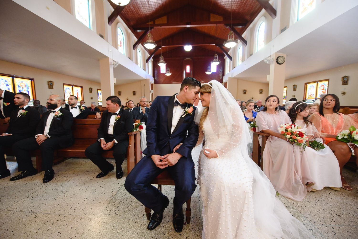 Bride and groom share a kiss at the altar during a church wedding ceremony with guests seated in pews.