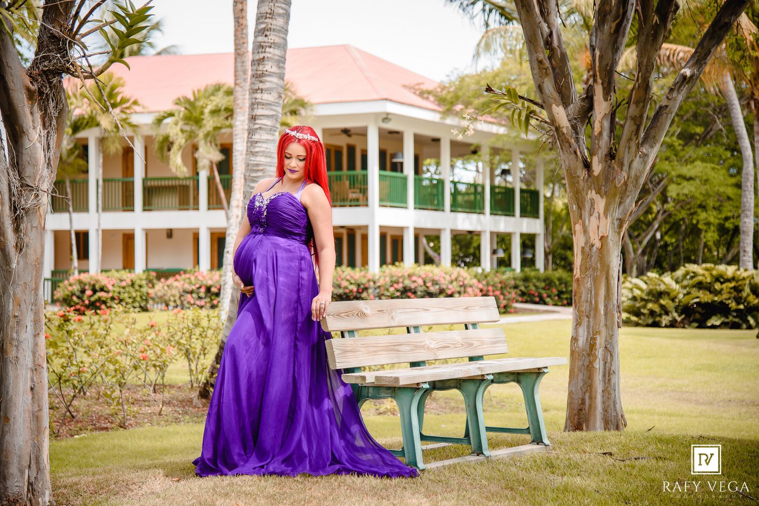 Woman in purple gown with red hair poses near bench at tropical estate during professional outdoor photo shoot.