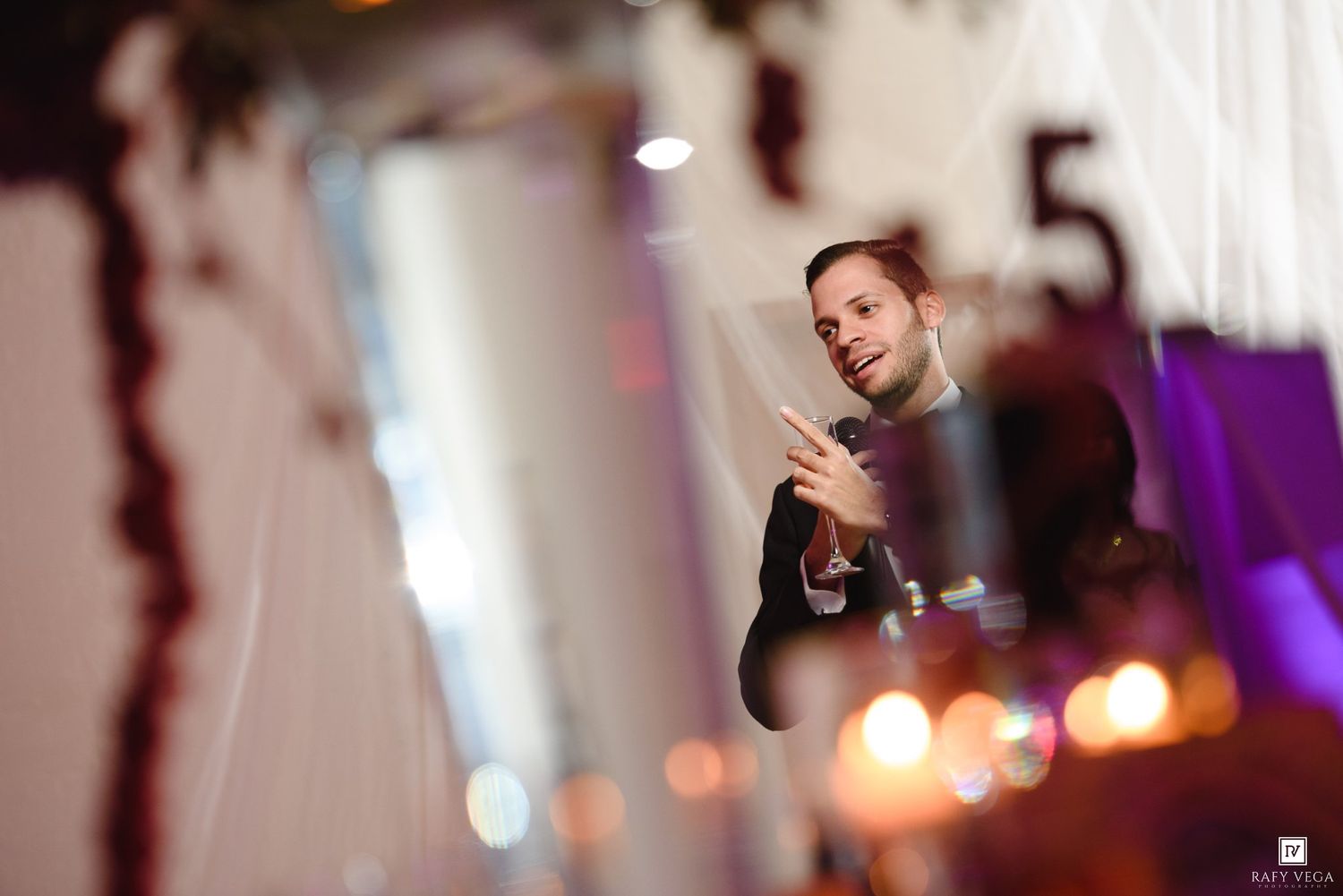 Wedding DJ or emcee speaks into microphone at elegantly decorated reception venue with bokeh lights.