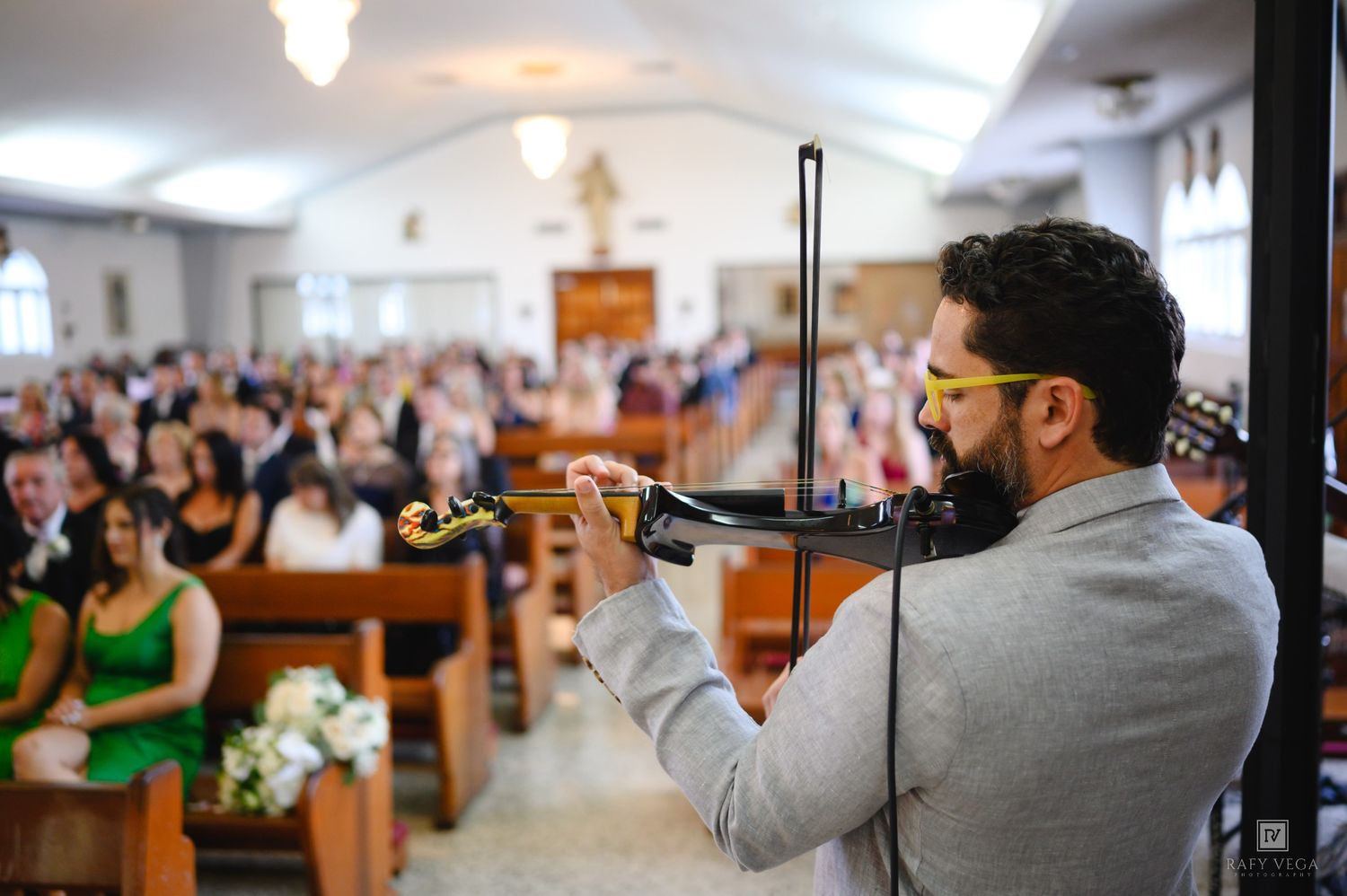 Violinist performing at a wedding ceremony in a church filled with guests seated in wooden pews.
