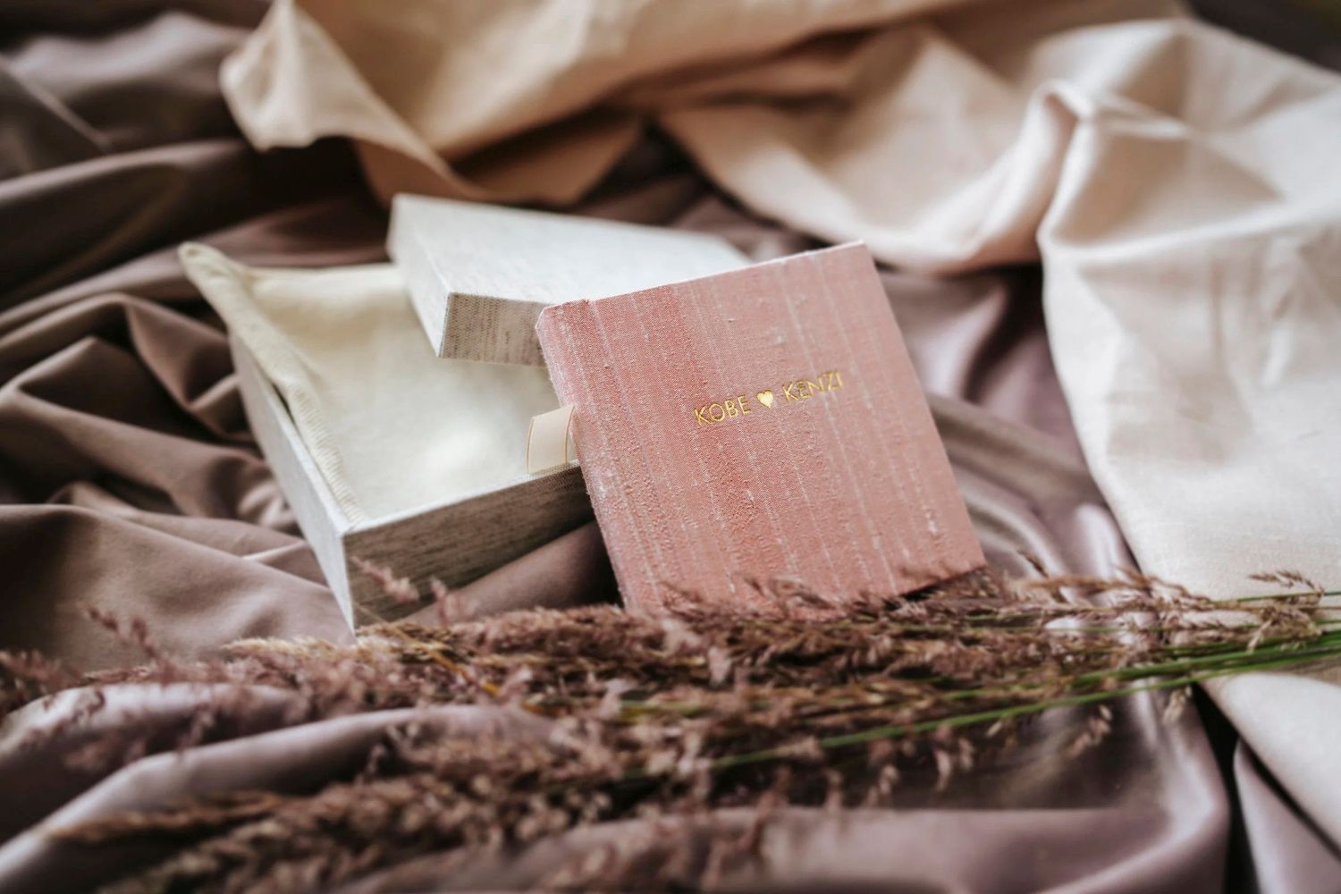 Pink velvet journal with gold lettering resting on silky fabric with dried lavender flowers.
