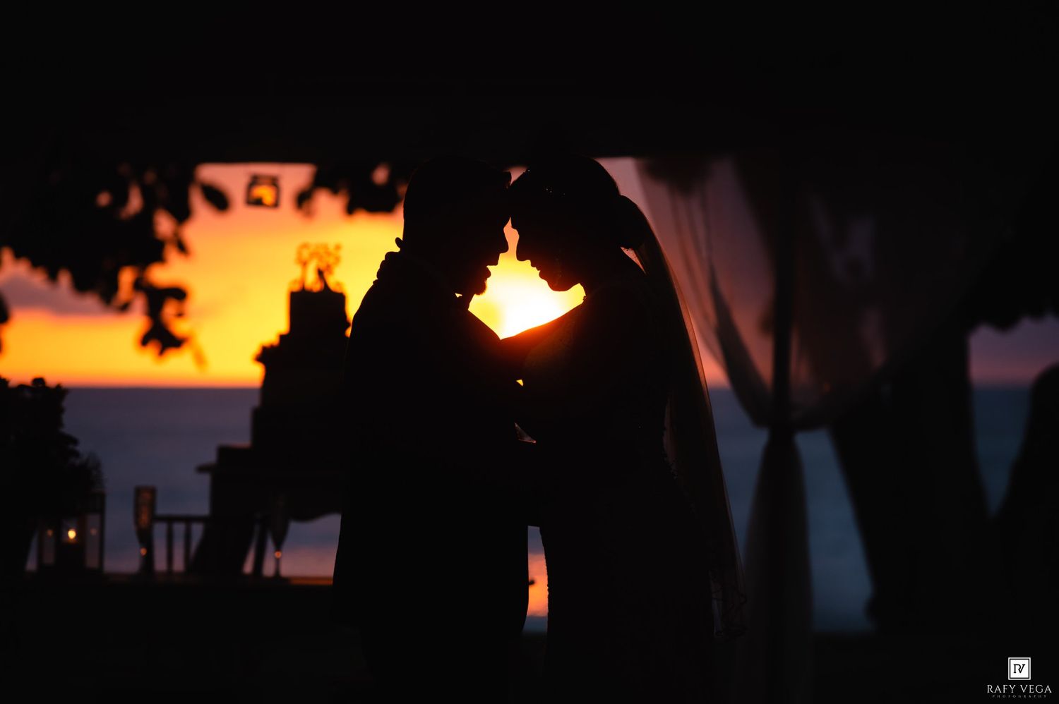 Silhouette of a couple sharing a romantic moment at sunset with golden orange sky in the background.