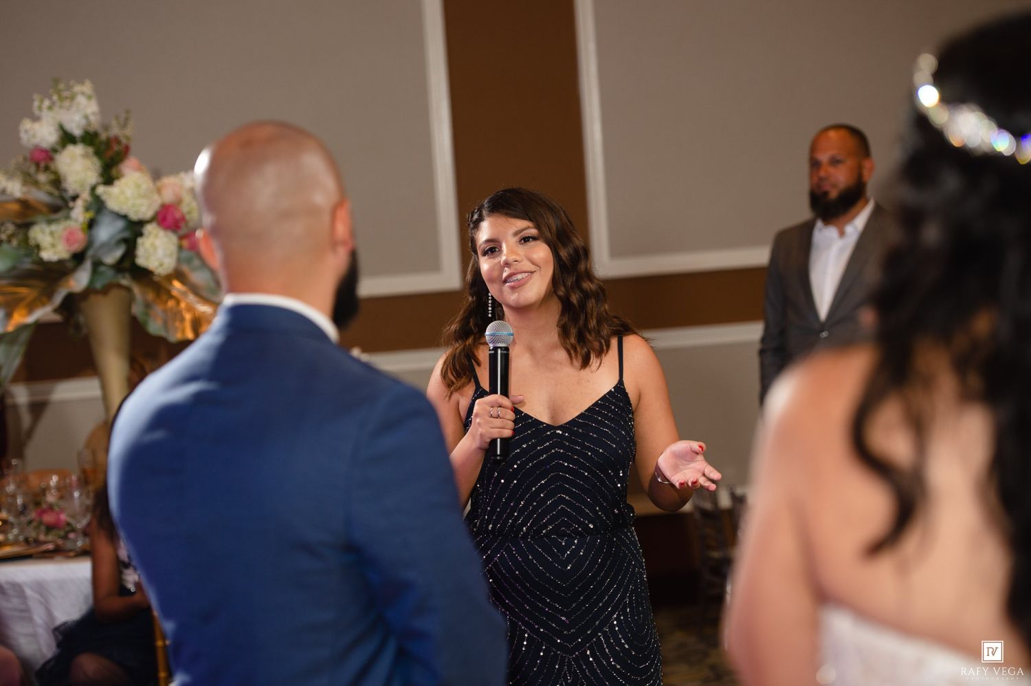 Woman in sequin dress gives a heartfelt speech at a wedding reception holding a microphone.