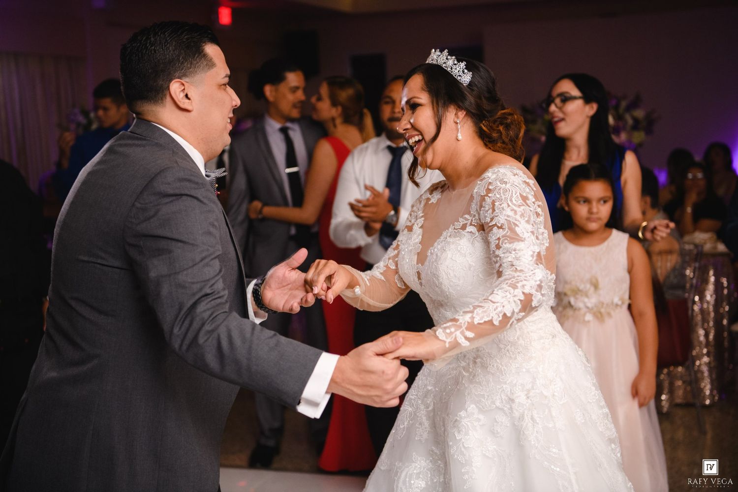 Smiling bride in white ball gown dances joyfully with groom at lively wedding reception celebration.