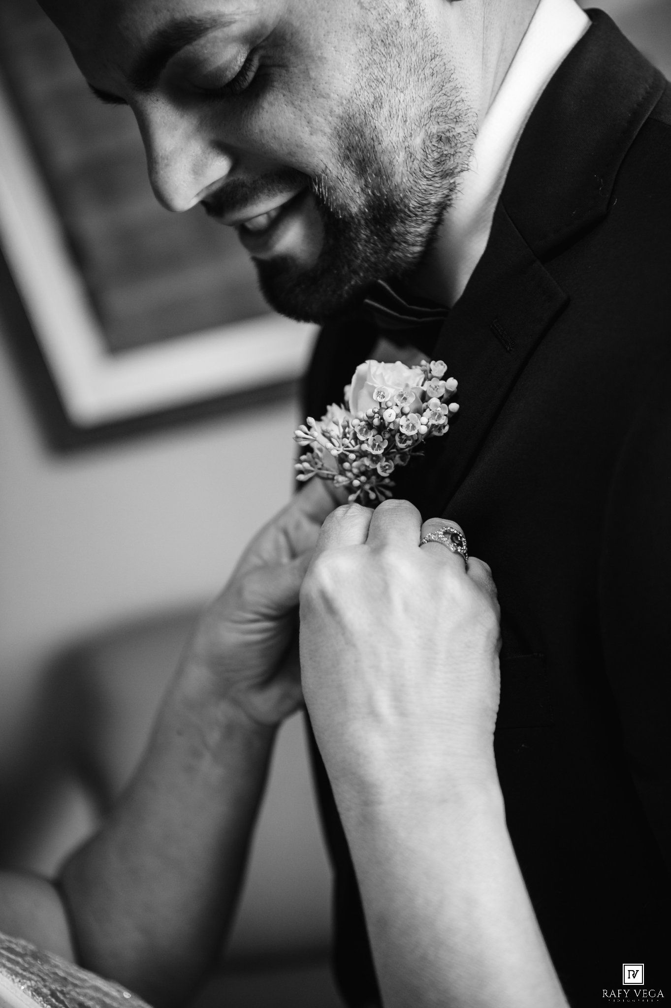 Black and white photo of a smiling groom having a floral boutonniere pinned to his suit lapel.