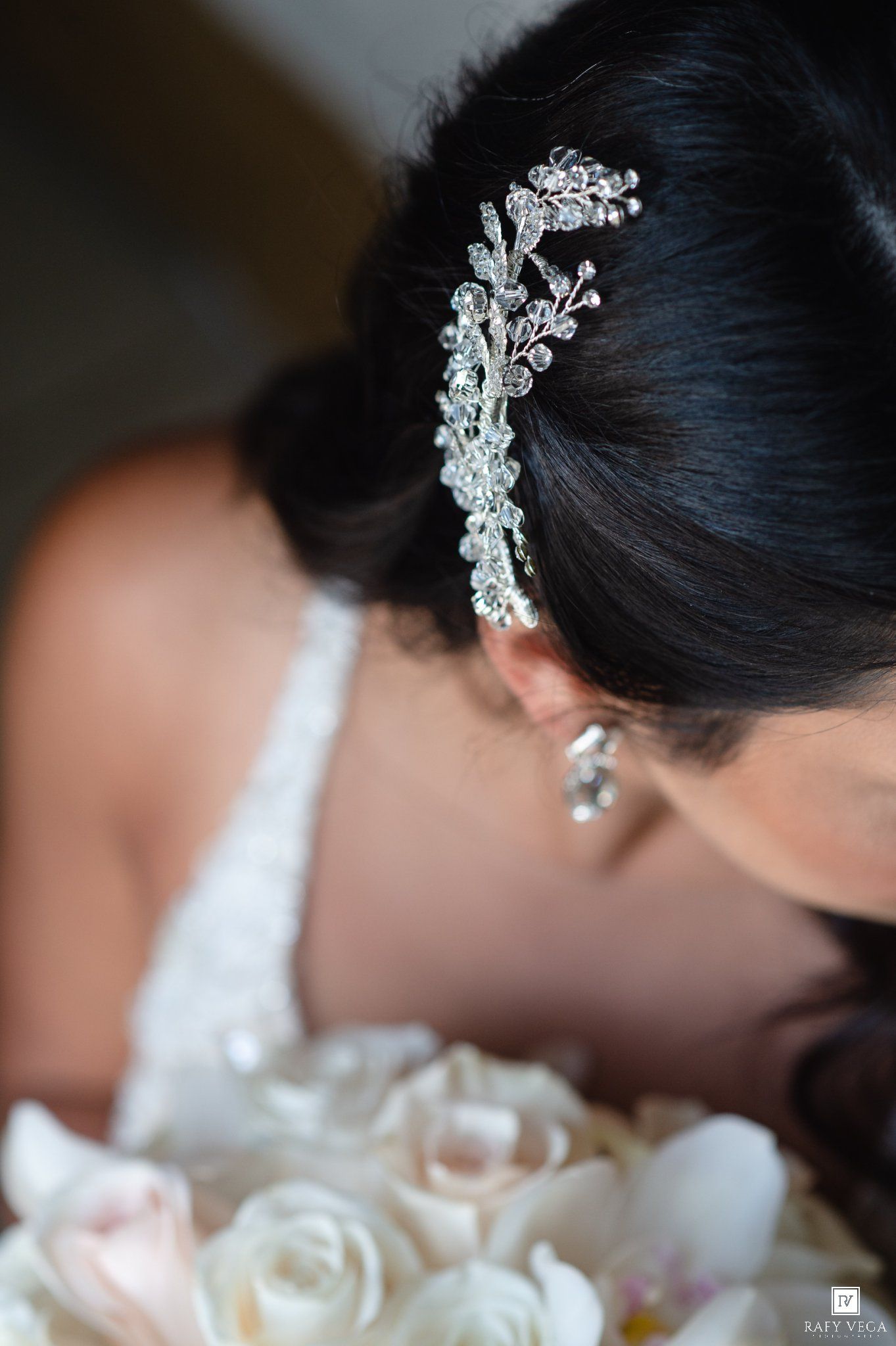 Bride wearing a sparkling crystal hair comb accessory with matching earrings, holding a white rose bouquet on her wedding day.