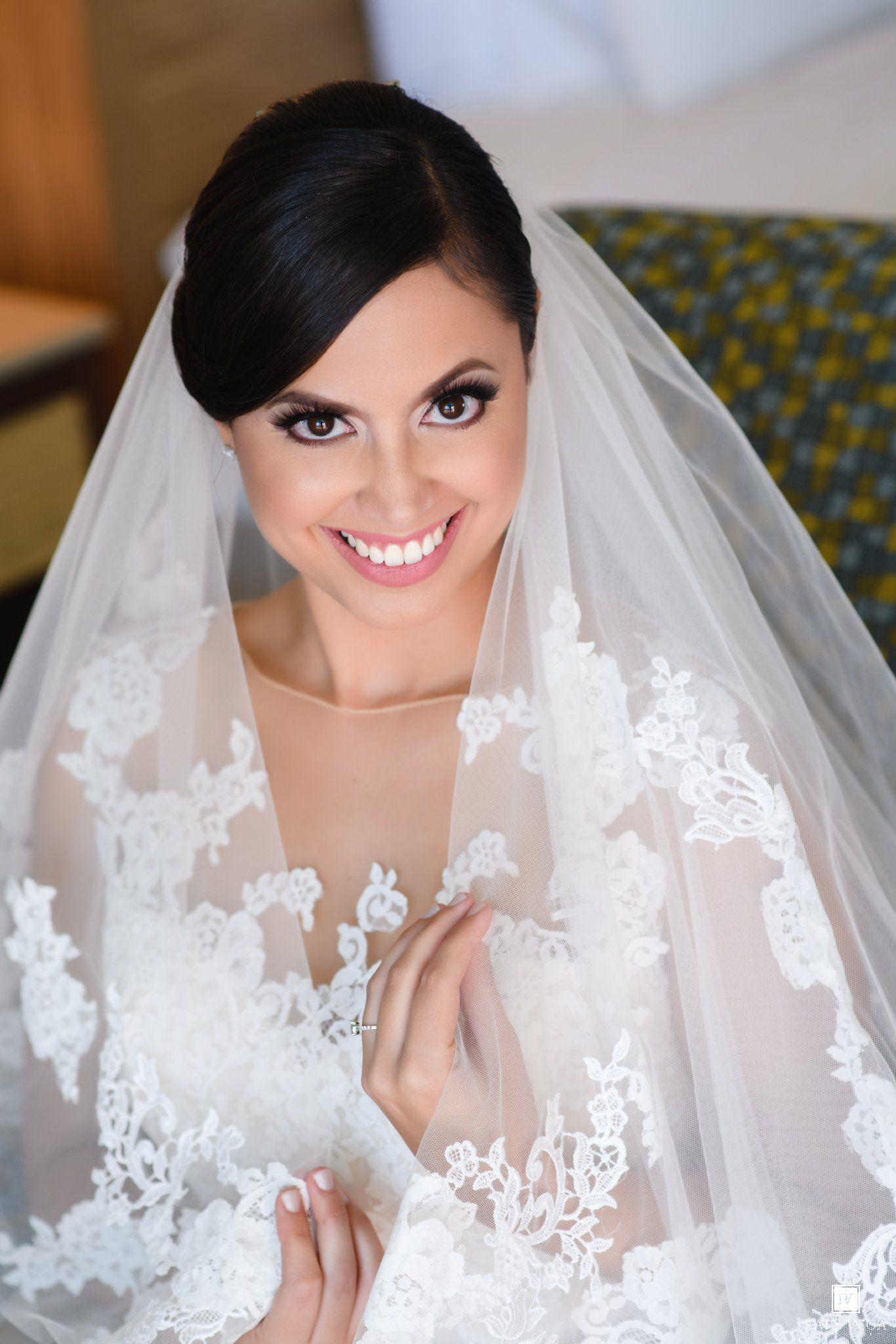 Smiling bride in white lace wedding dress and veil with elegant updo hairstyle and dramatic eye makeup.