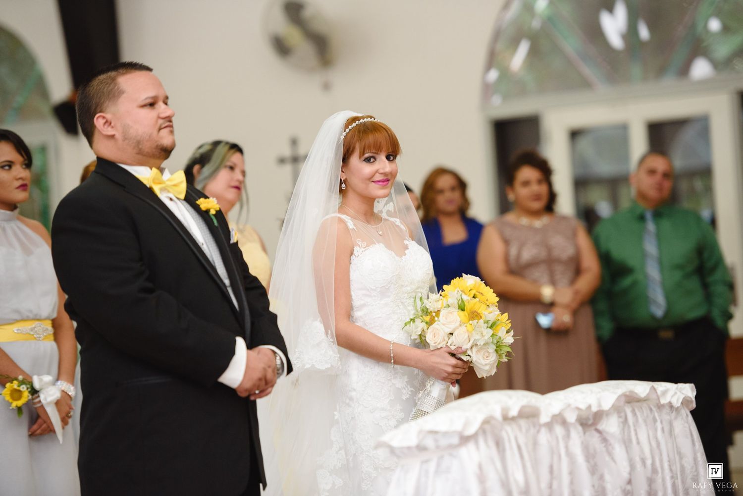 Bride and groom exchanging vows at church altar, bride holding yellow and white bouquet.