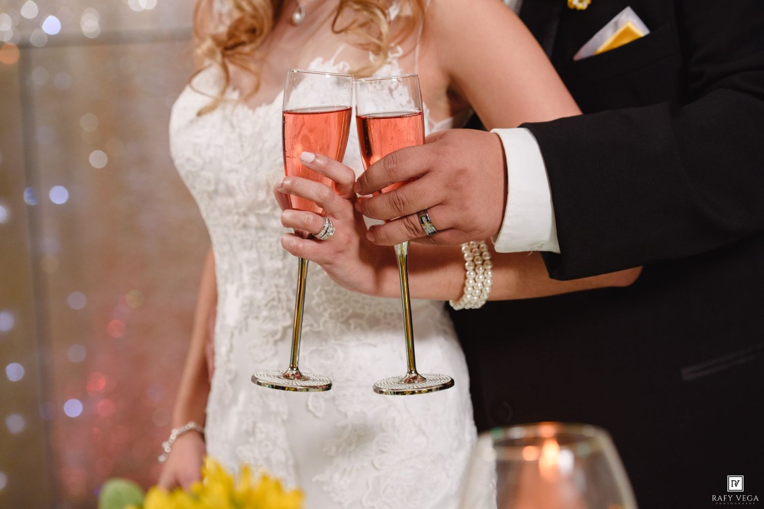 Bride and groom clinking gold-rimmed champagne glasses filled with pink bubbly at their wedding reception.