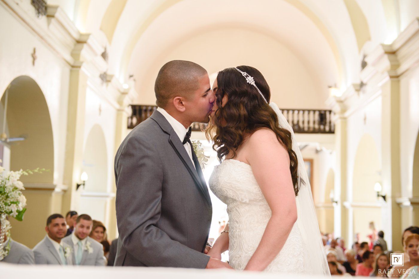 Bride and groom share first kiss at church altar during wedding ceremony.