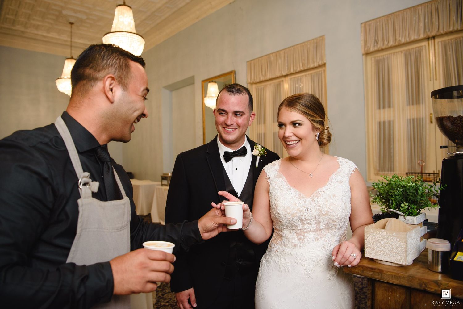 Bride and groom smile while receiving coffee from a catering staff member at their wedding reception.