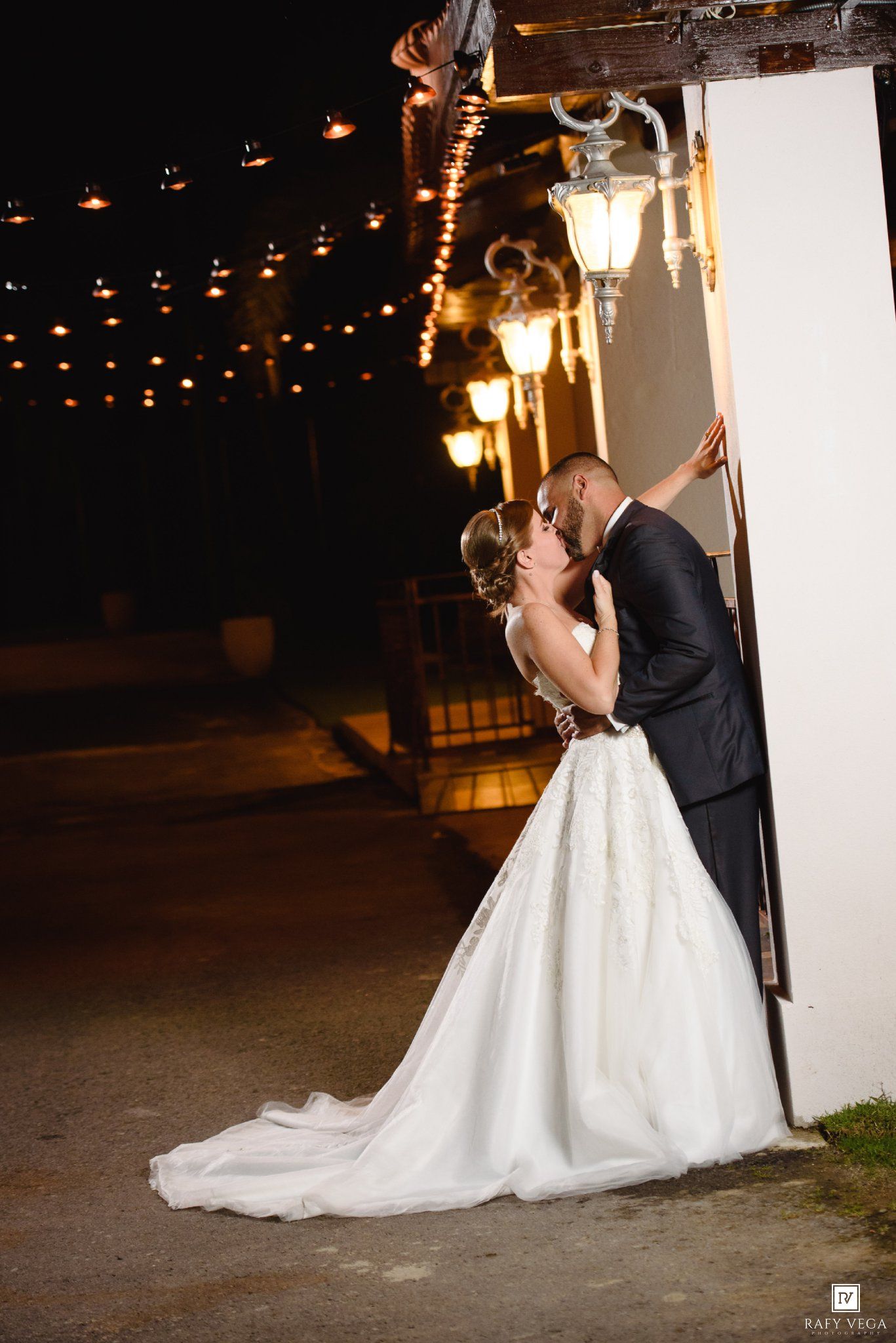 Bride and groom share a romantic kiss by glowing lanterns and string lights at their outdoor night wedding.