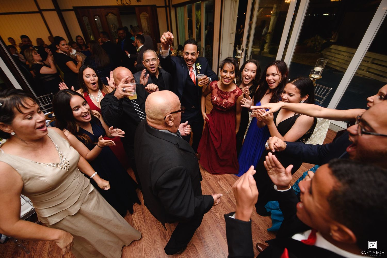 Guests dancing in a circle at a lively wedding reception party indoors.