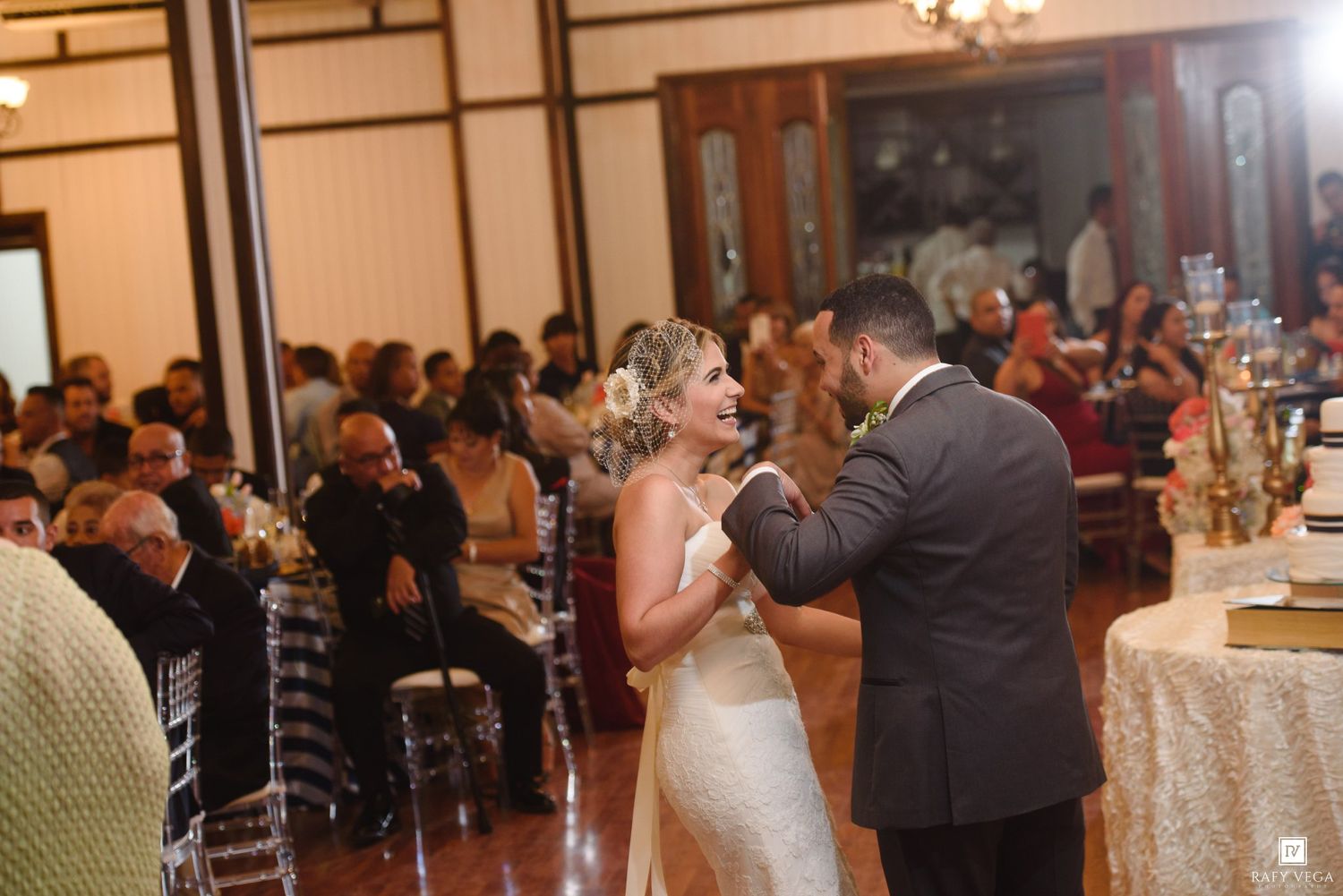 Bride and groom share first dance at elegant wedding reception with guests seated at tables.