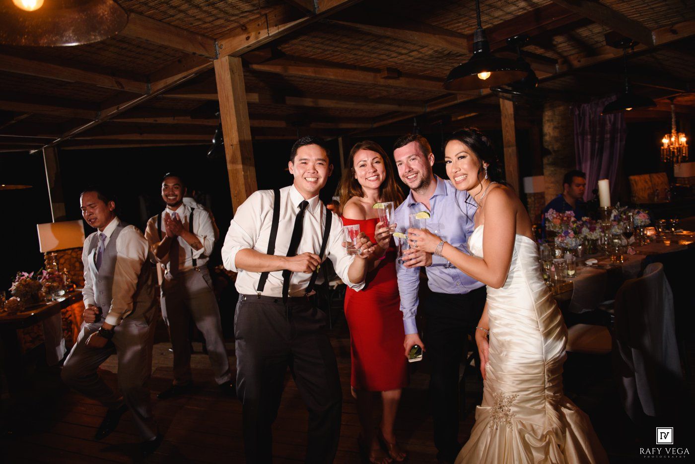 Wedding guests pose and smile at a lively indoor reception venue at night.