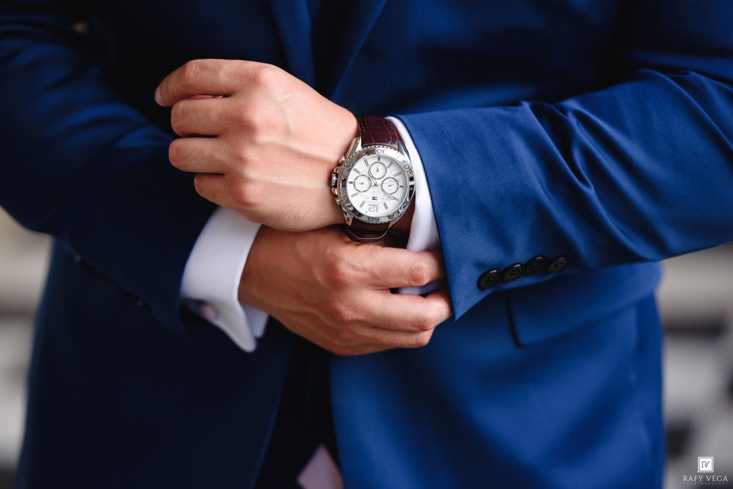 Man in blue suit adjusting a luxury chronograph watch on his wrist, elegant formal attire.