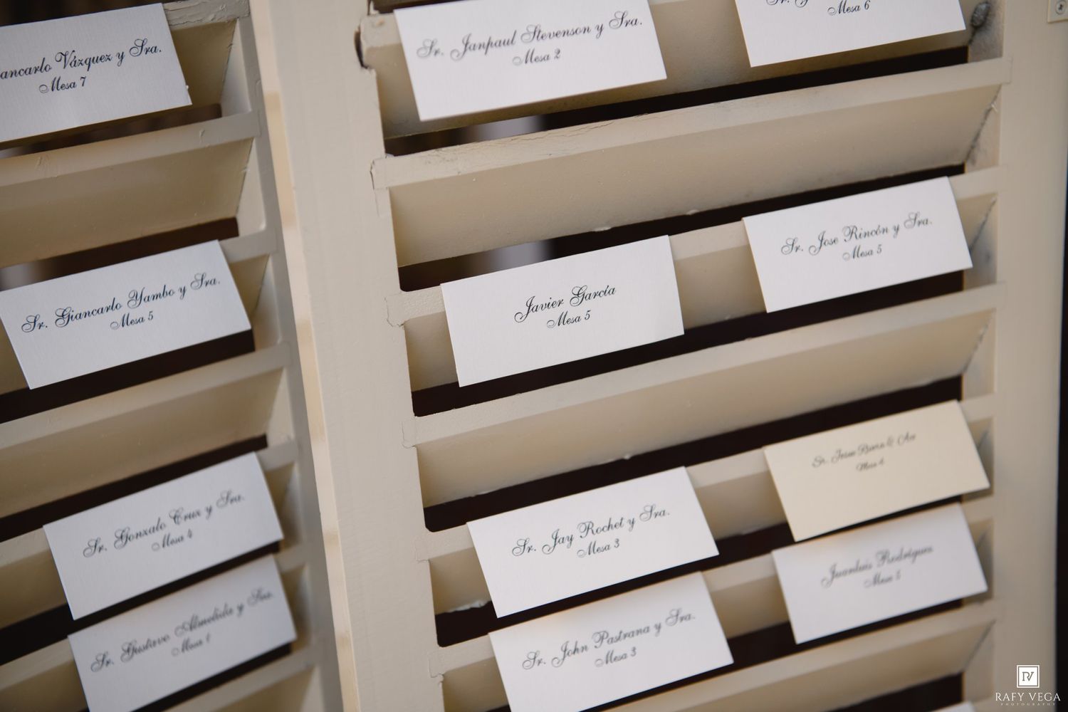 Elegant wedding seating chart cards displayed on a wooden shutter board with calligraphy guest names and table numbers.